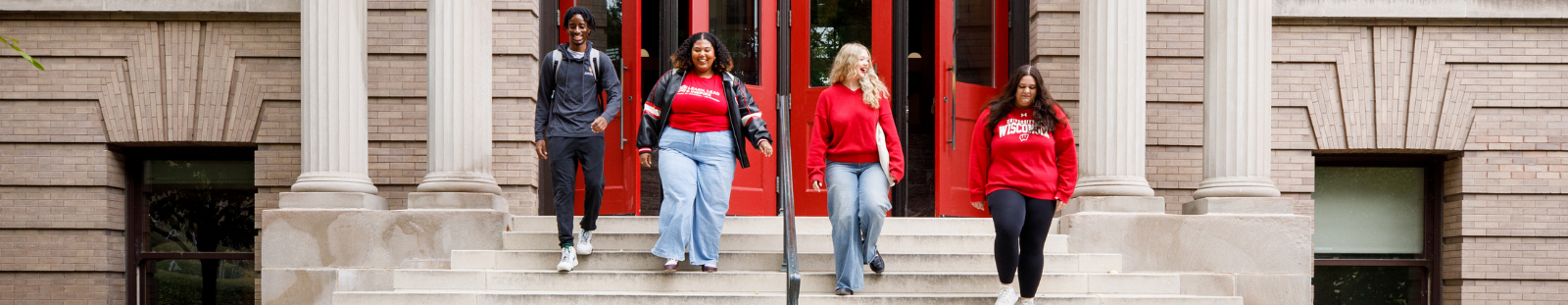 Four students walk down the stairs outside of a building with red doors